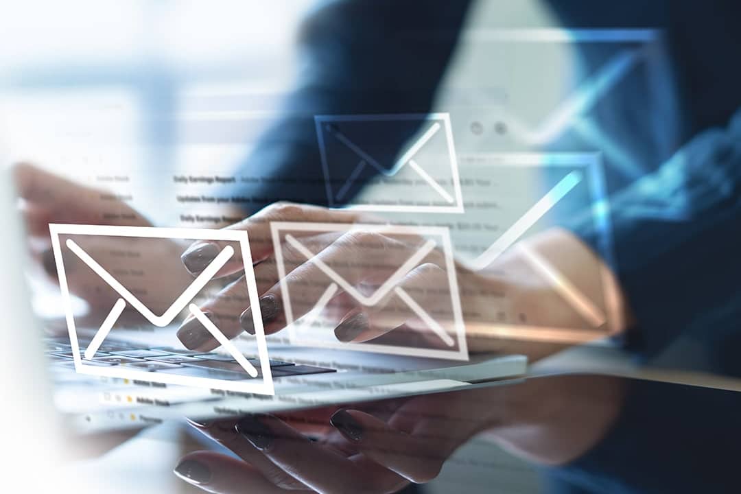A digital overlay of envelope icons appearing over an office professional typing from a laptop, signifying email and newsletter updates.